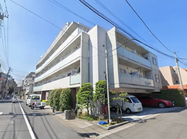 - 現代的なデザインのマンション外観、青空を背景にした四階建ての建物、周囲に植栽や車が駐車している様子
