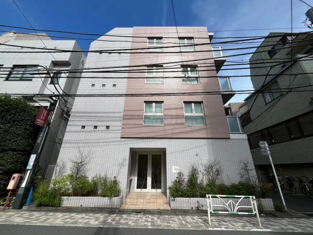 - モダンなデザインの外観を持つ建物、グレーとピンクのタイルで覆われたファサード、青空と電線が見える街並みの風景