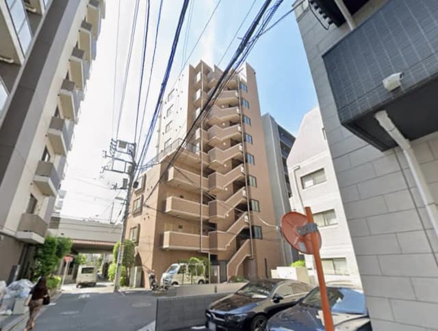 - 都市の住宅街に位置するモダンなアパートビル、近くには駐車場と電線が見える風景