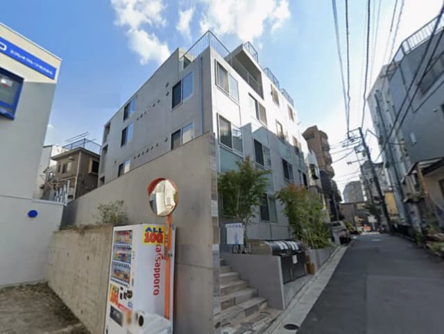 - コンクリート打ちっぱなしの近代的なアパートメントビル、屋根にバルコニー、近くに自動販売機と街路がある風景