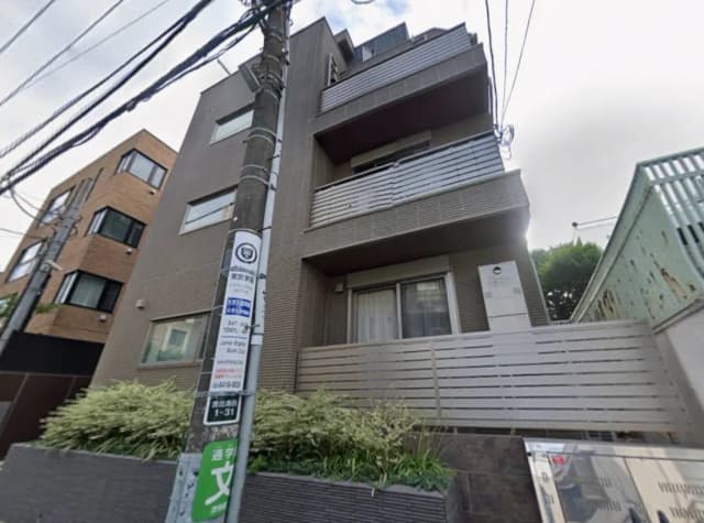 - モダンなデザインの4階建てアパートメント、シンプルな外観とグリーンが施されたエントランスエリア、周囲に並ぶ建物が特徴的な街並み