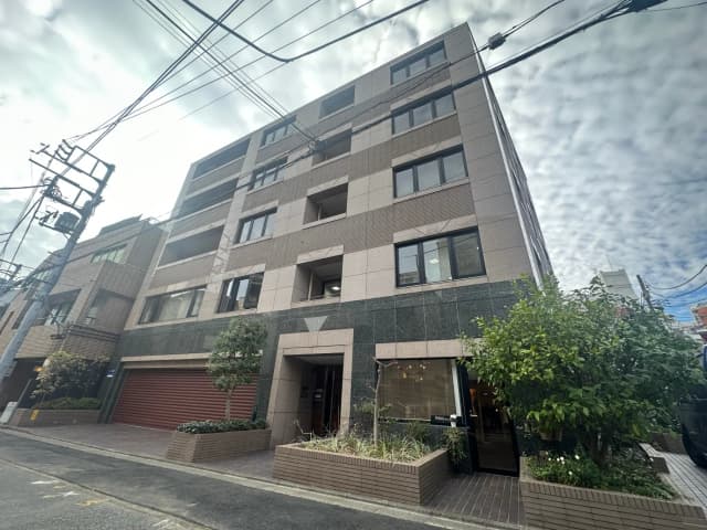 現代的な外観の都市型マンション、植栽付きのエントランス、青空と電線が交差する街並み