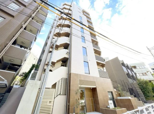 - 現代的な外観の6階建てのマンション、明るい空の下で周囲の建物と調和したデザイン