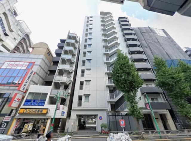 - 都市に立つモダンな高層マンションの外観、周囲に商業施設や樹木がある通りの風景