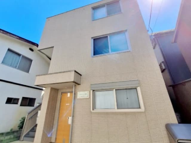 - シンプルでモダンな外観の3階建て住宅、明るい青空を背景に、正面のエントランスと窓が特徴的なデザイン
