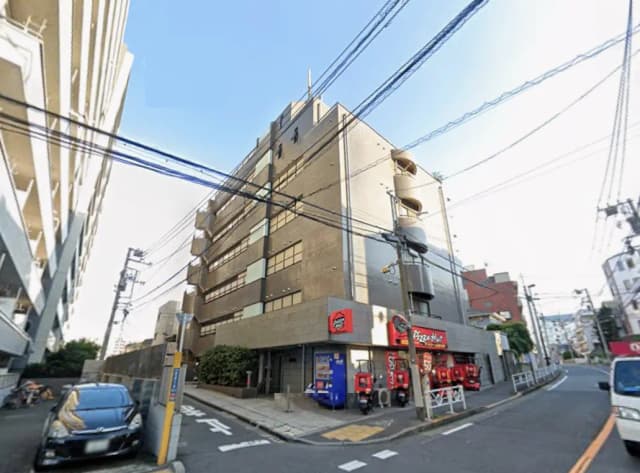 - 近代的な外観のビルとピザのデリバリー店舗、周囲に電柱と配車が並ぶ街並みの風景