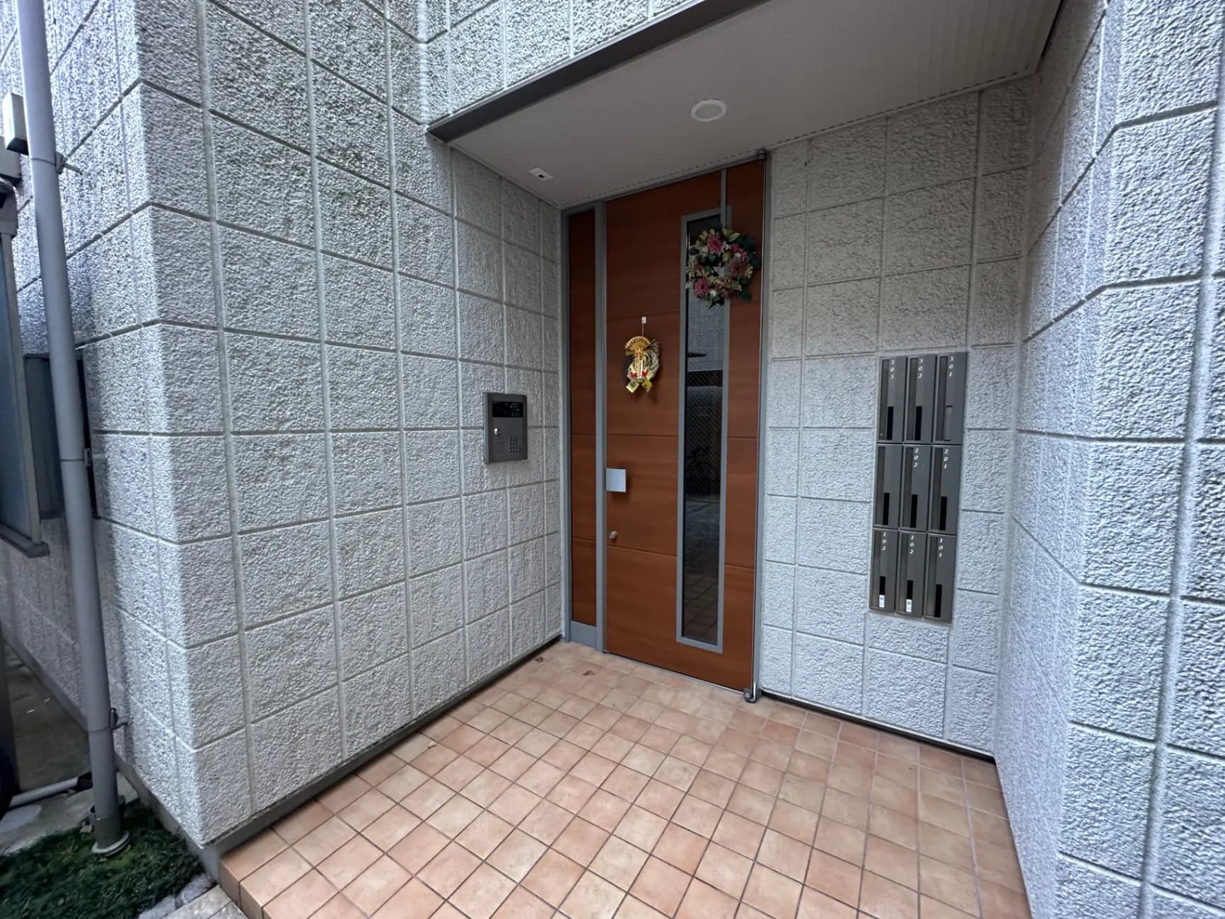 現代的な外観のエントランス、タイル張りのアプローチ、木製ドアにリース、郵便受けとインターフォン付き