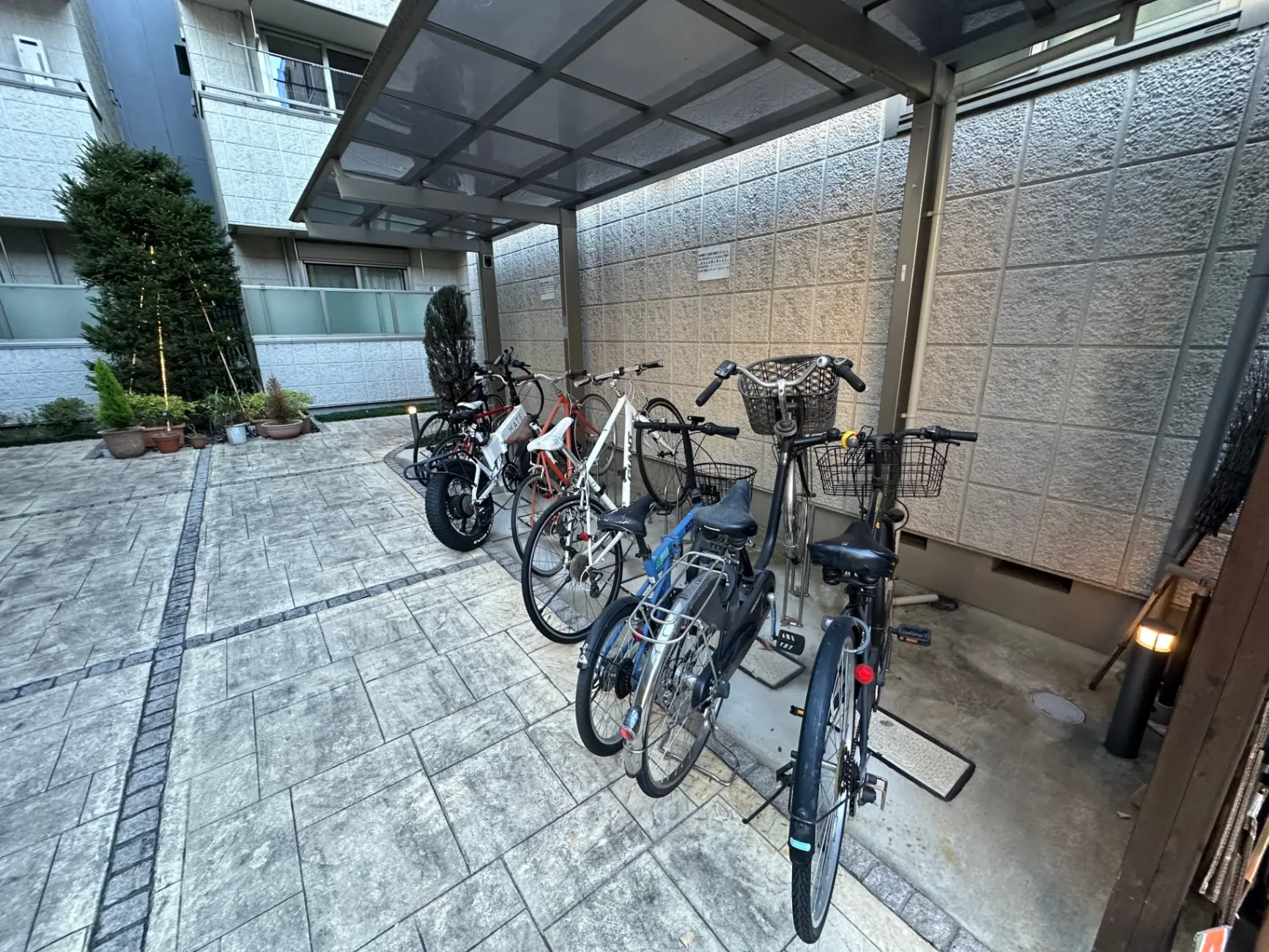 マンションの屋根付き自転車駐輪場、整然と並べられた様々な自転車、背景に緑の植木