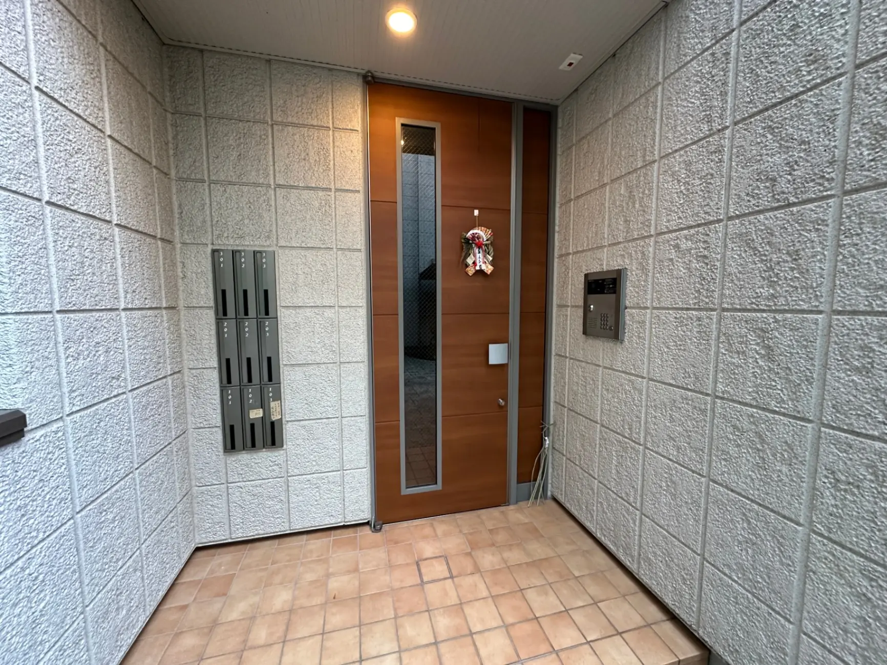 モダンなエントランス、タイル張りの床、インターホンと郵便受けが備わった玄関ドア