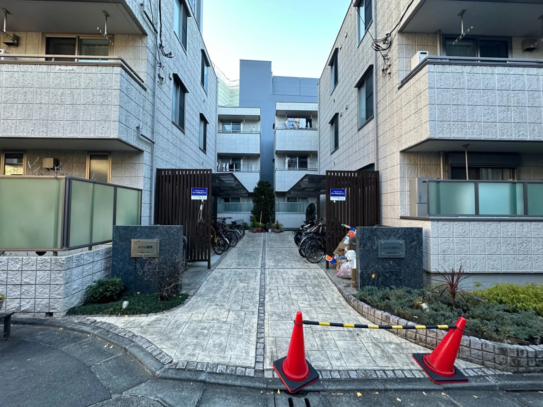 住宅街のアパートの入り口、舗装されたアプローチ、駐輪スペースあり、午後の日差し