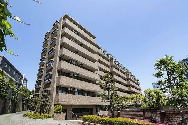 - 近代的なデザインのマンションの外観、明るい青空の下に立つ6階建ての建物と周囲の緑豊かな landscaping