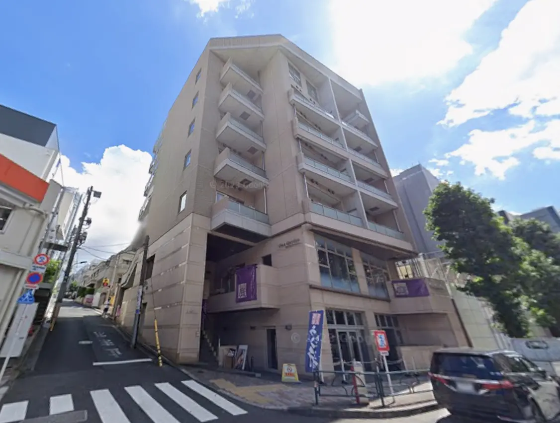 - 住宅街に立つモダンなマンションの外観、日差しが差し込む晴れた空、周囲の自然や街並みが見える景色