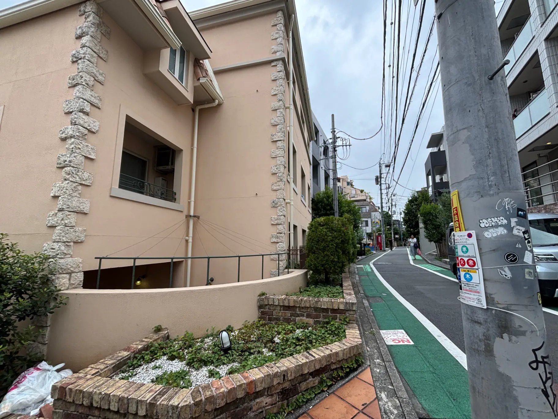 - 鉄筋コンクリートの外壁を持つ住宅、植栽と石造りの花壇、電線と道路が見える静かな街並みの風景