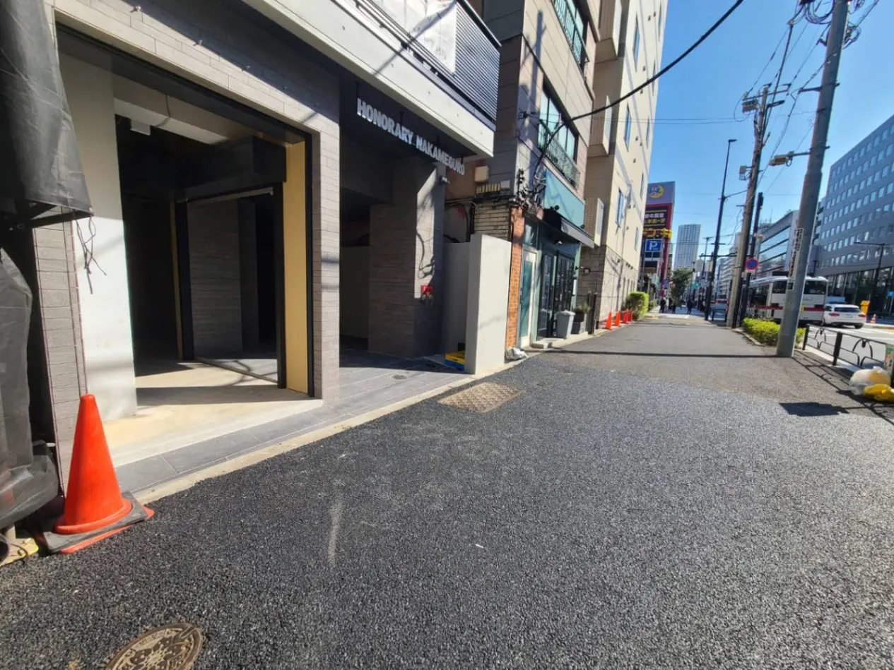 都市の通り沿いにある現代的な建物のエントランス、晴れた日差しと影、歩道と道路