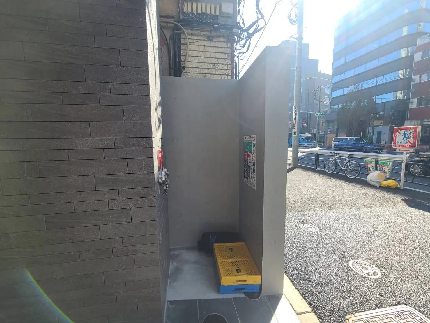 日差しが差し込む都市の歩道と、ゴミが散らかった公衆電話ボックス