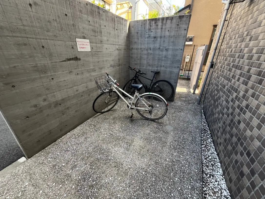 コンクリートの壁に囲まれた屋外の自転車置き場、白と黒の自転車が停められている光景