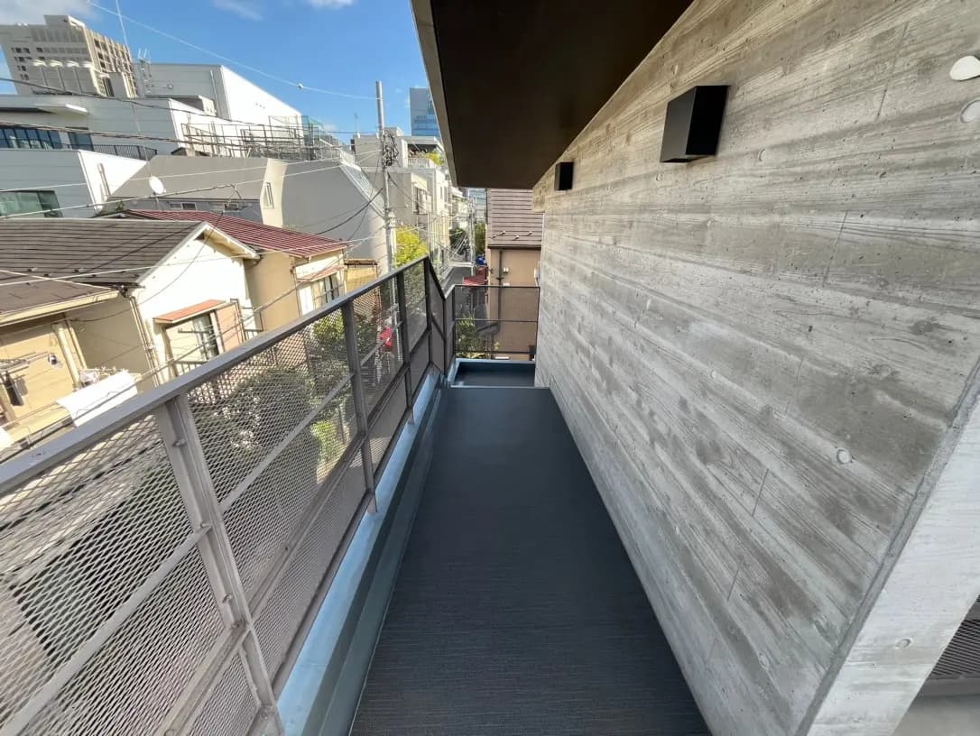 都会的な風景が見えるモダンなバルコニー、コンクリートの壁面、メッシュの手すり