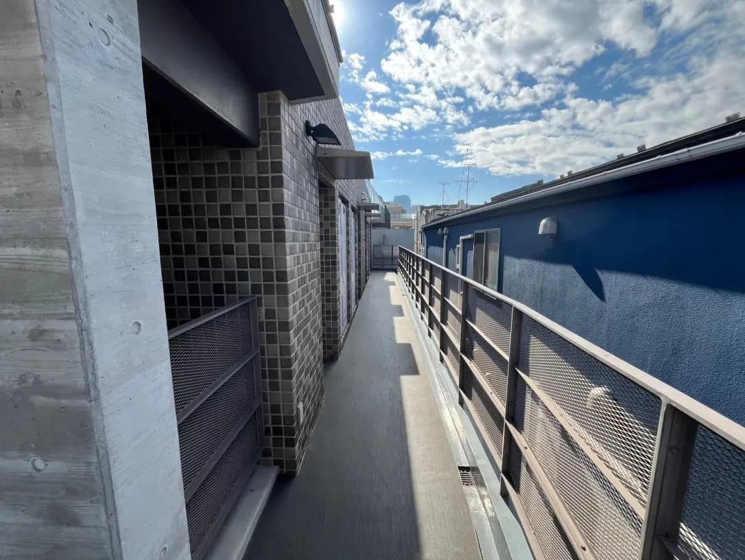 青い壁の現代的なアパートの外廊下、コンクリートとレンガのディテール、都市のスカイラインと晴れた空