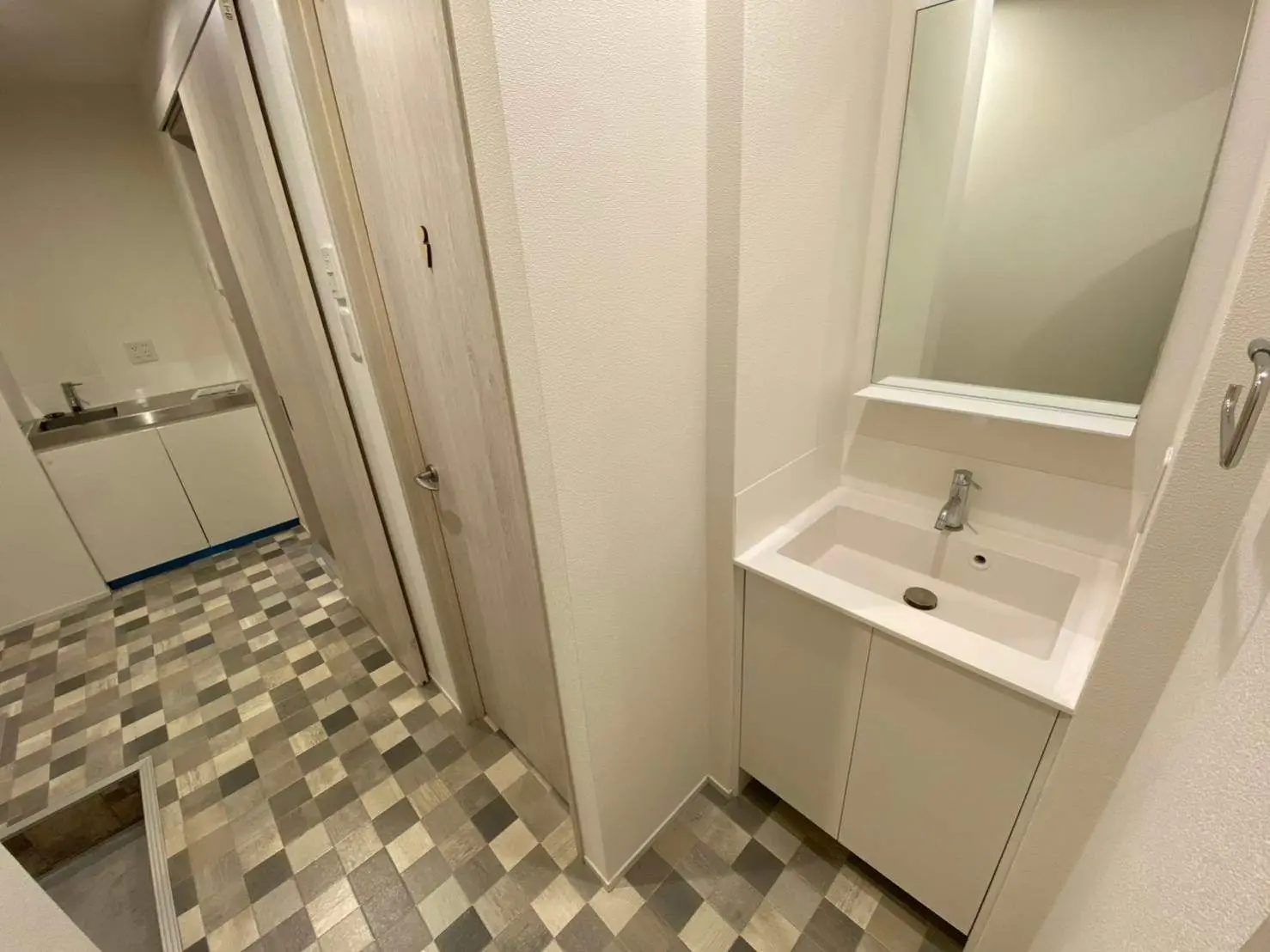 シンプルなデザインのバスルーム、チェック柄の床タイル、壁に取り付けられた洗面台と鏡