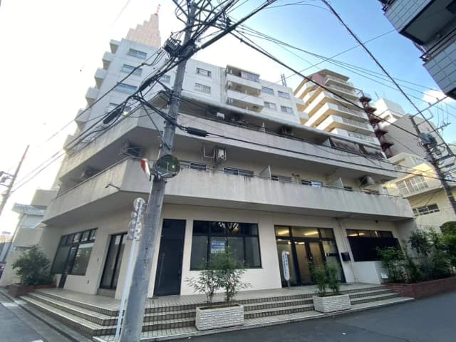 都市型マンションの外観、多くの電線が交差する街並み、青空の下での日差し