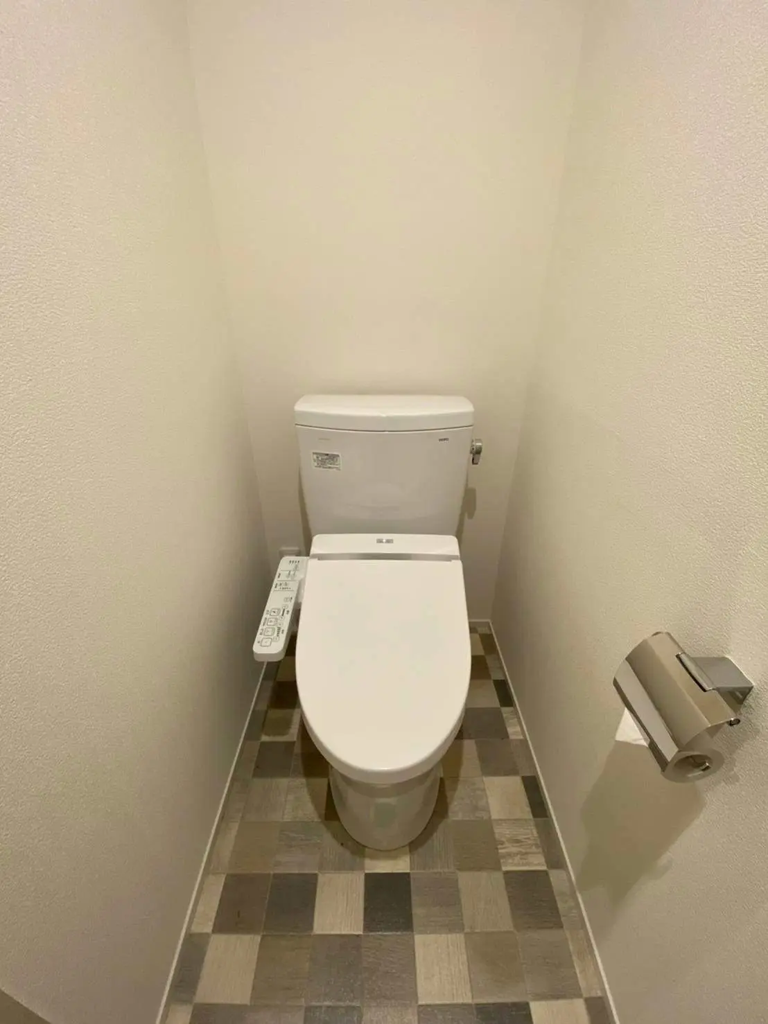 シンプルでモダンなデザインのトイレルーム、ウォシュレット付きの白い便器と茶色系のタイルフローリング