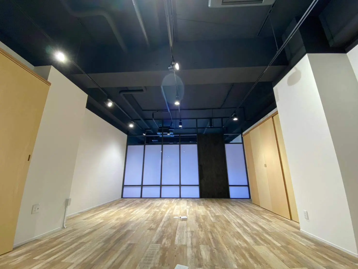 モダンで広々としたオフィス空間、木目調フローリング、天井に埋め込まれた照明、大型ガラス窓