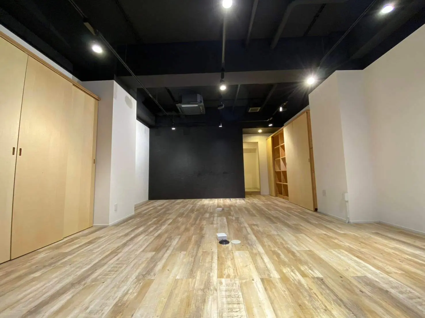 空間広々としたモダンなオフィス空間、木目調のフローリングとブラック天井扉付き収納キャビネットが備わるインテリアデザイン