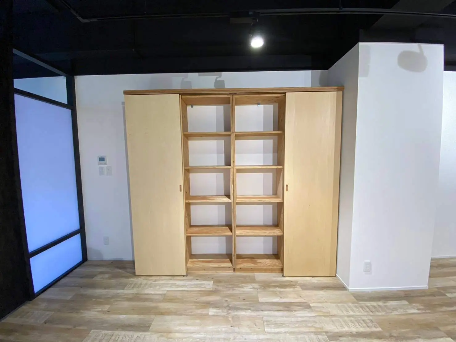 モダンな木製の建具と収納棚が付いた洋室、白い壁と木目調のフローリングが特徴的なインテリア