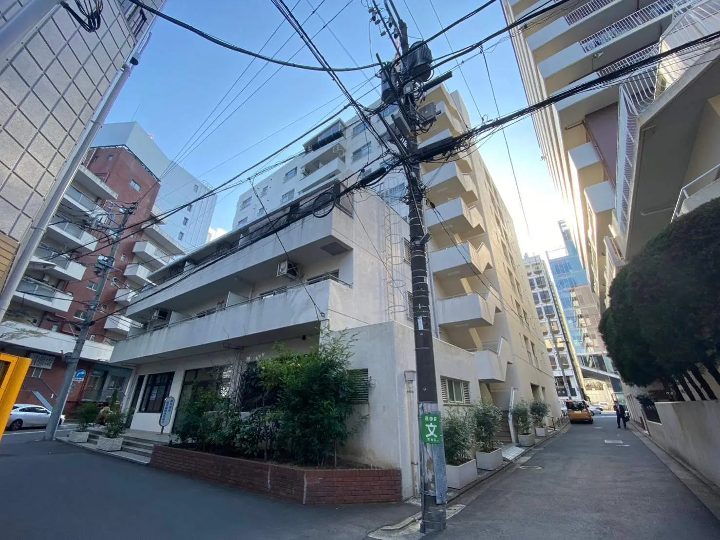 都会の住宅街、道路沿いに並ぶ電柱と配線、昼間の晴天の下のアパートメントビル