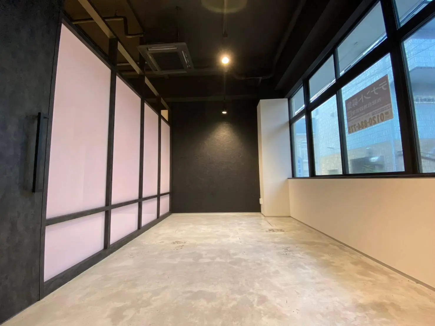 モダンなインダストリアルデザインのショップスペース、コンクリートフロアと黒い壁、大きな窓から明るい光が差し込む店内