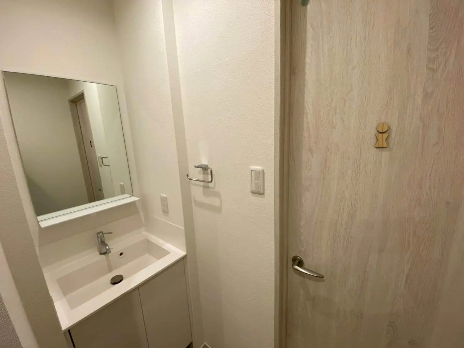 シンプルでモダンなデザインの洗面台、鏡と収納スペースがある木製の扉、明るい壁のカラーのバスルームインテリア