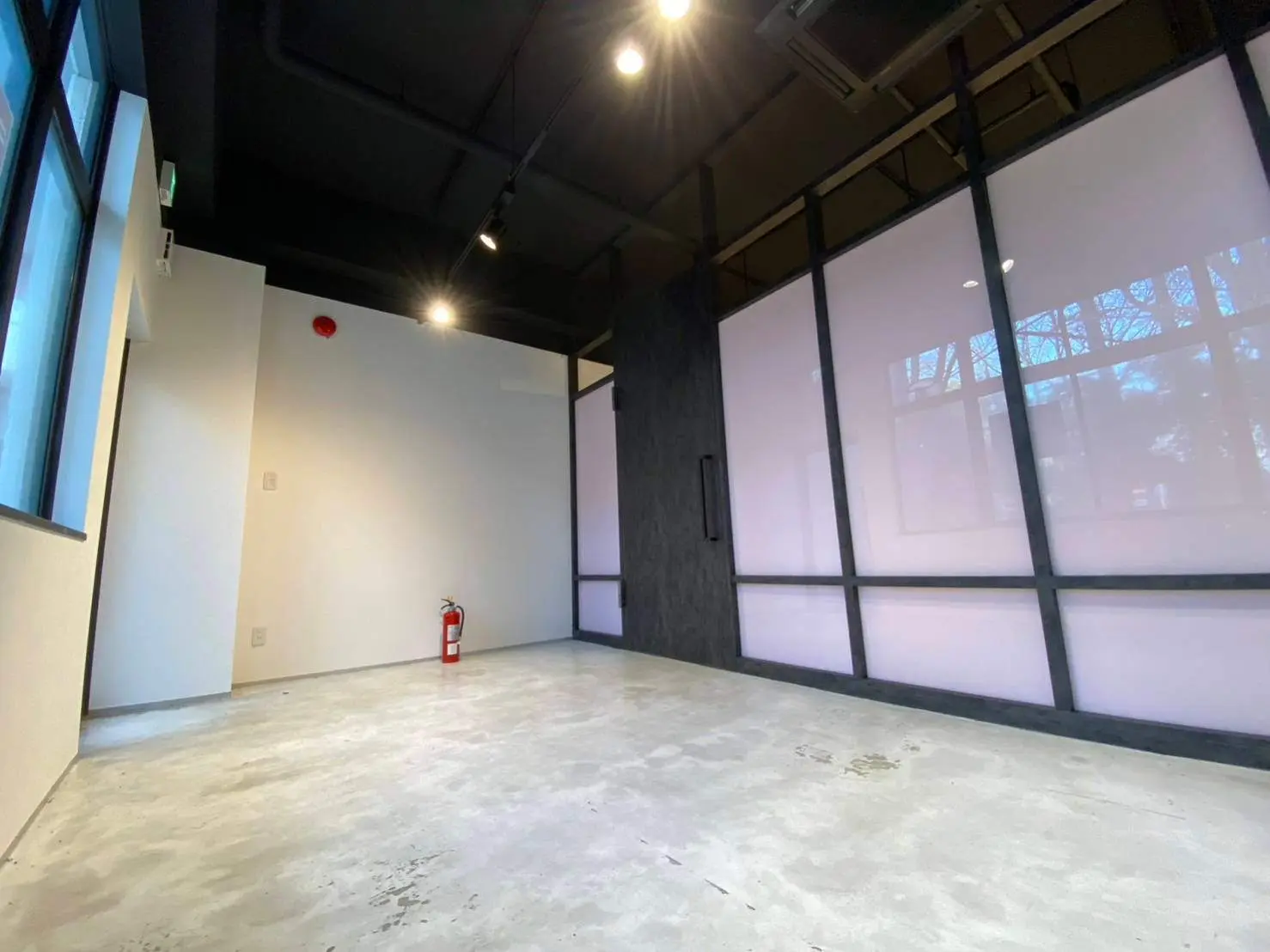 空白のオフィススペース、黒い天井とグレーの床、大きな窓から光が入る室内