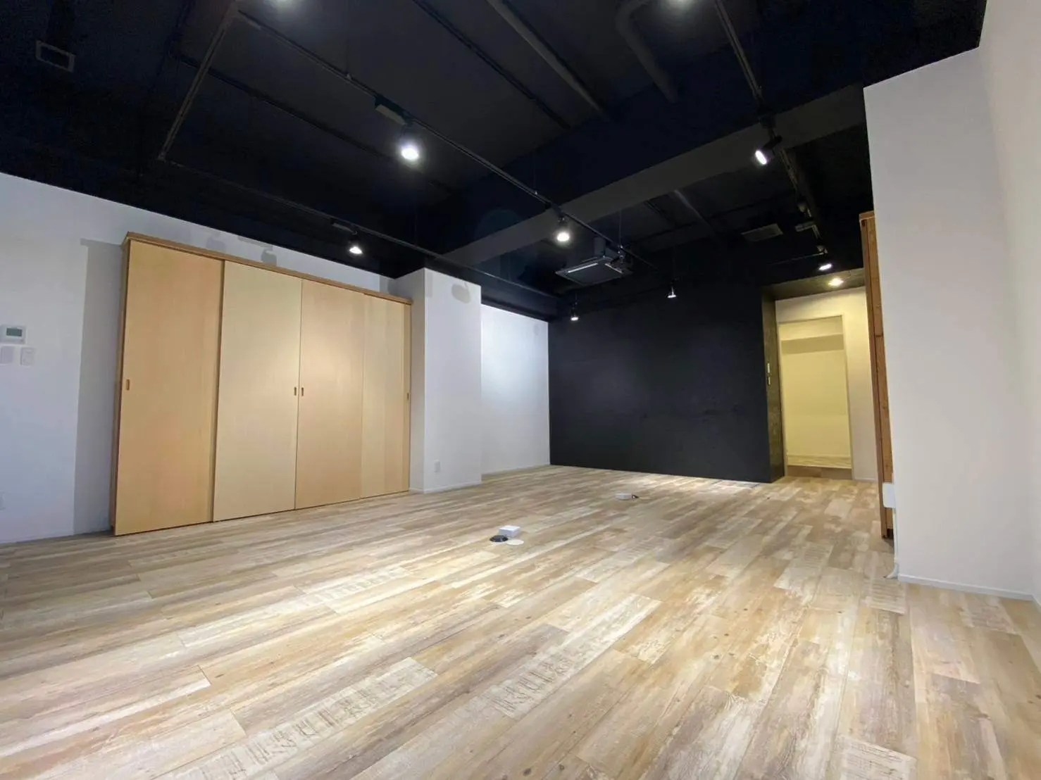 広々としたオフィススペース、木目調のフローリング、シンプルな収納クローゼット、ダークカラーの天井とスポットライト