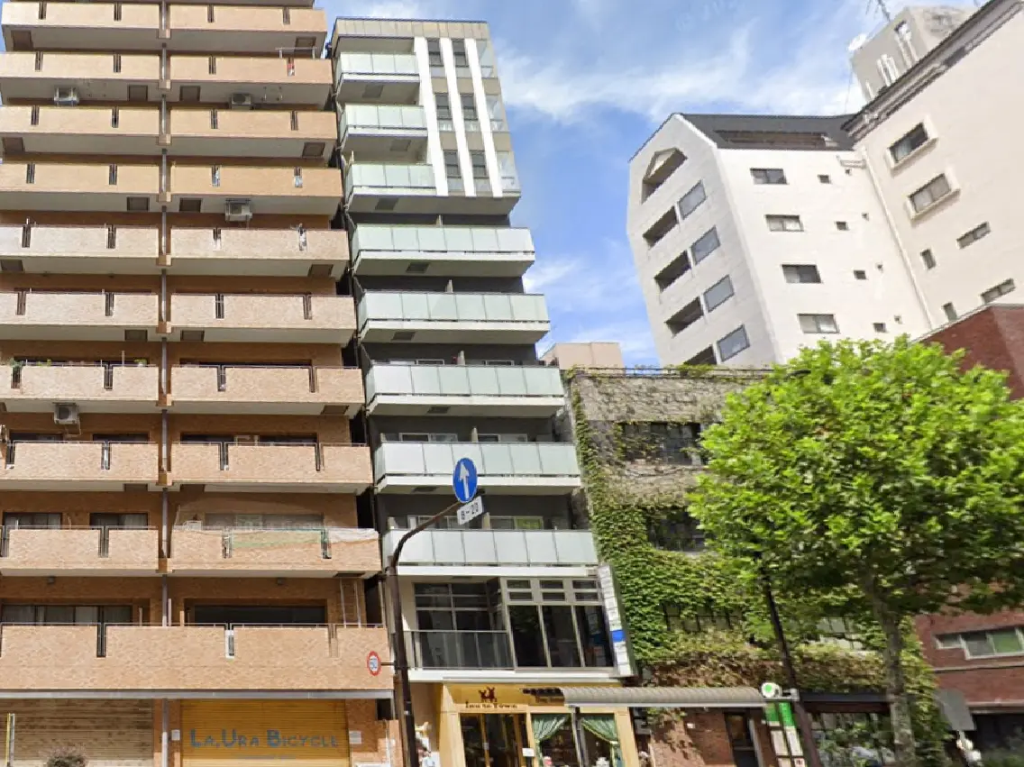 - 近代的なアパートメントビルの外観、ガラスバルコニーを持ち、隣には緑の壁を持つ古い建物と道標が見える街の景観