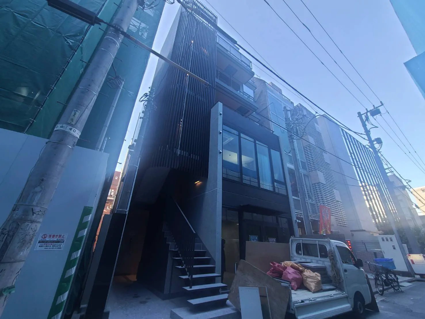 - 近代的なビルの外観、階段と黒いファサード、周囲の建物と電信柱が映る都市景観