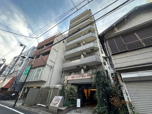 都市の通りに面したマンションと古い住宅、青空と電線が交差する風景