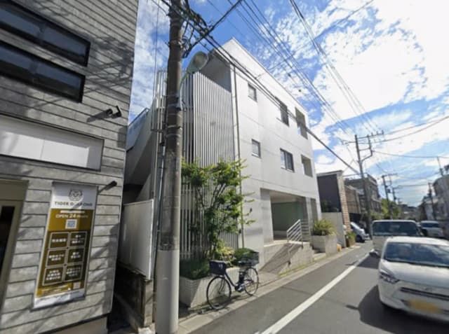 - 白を基調としたモダンな建物の外観、通りに面した緑豊かな植栽、自転車が停まっている街並みの風景