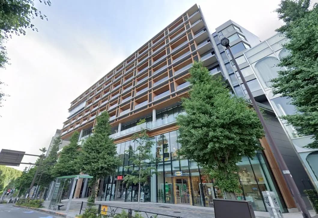 都市の景観に溶け込むモダンな外観のマンション、ガラス張りのエントランス、周囲に緑豊かな木々