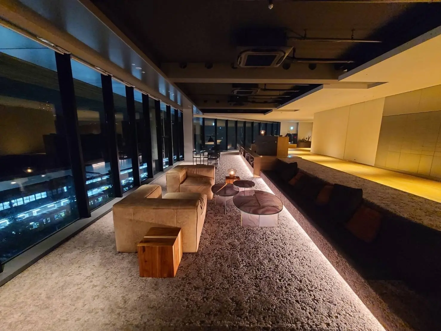 高層ビルの夜景を望むラグジュアリーなラウンジ、おしゃれなソファとオットマン、間接照明の落ち着いた雰囲気