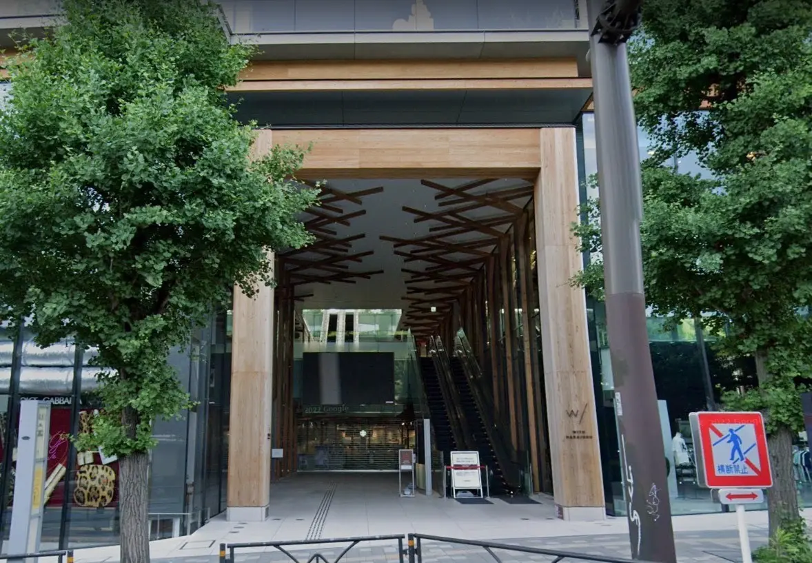 モダンで洗練された建築デザインのエントランス、木材とガラスを使用した外観デザイン、エスカレーターと緑豊かな植栽