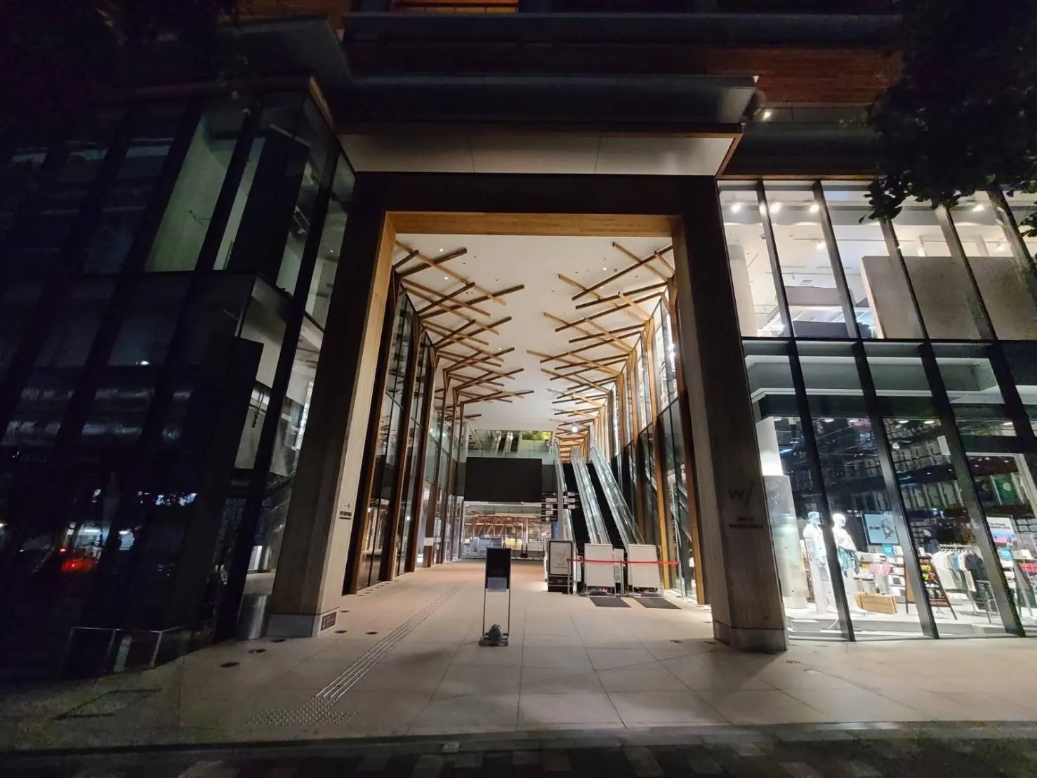 夜景のモダンなビルの外観、ガラス張りと木材でデザインされた広々とした通路