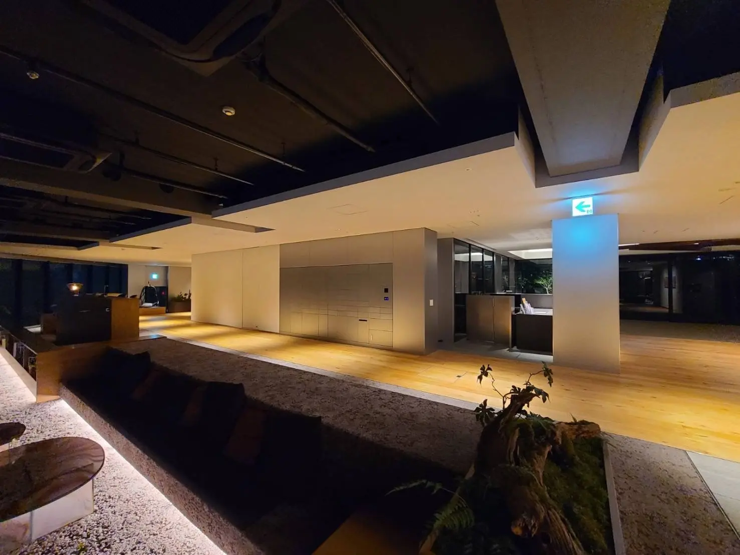 モダンなオフィスのエントランス、木製フロアと植物の装飾、落ち着いた照明のある空間デザイン