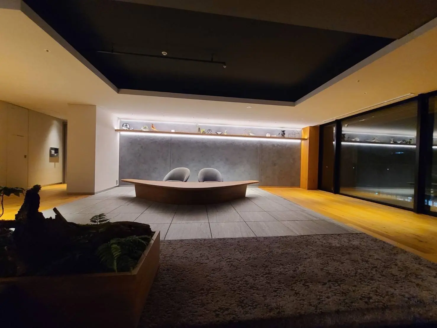 モダンなリビングルームのインテリア、暖色の照明、グレーの壁、大型の窓と床に敷かれたラグ