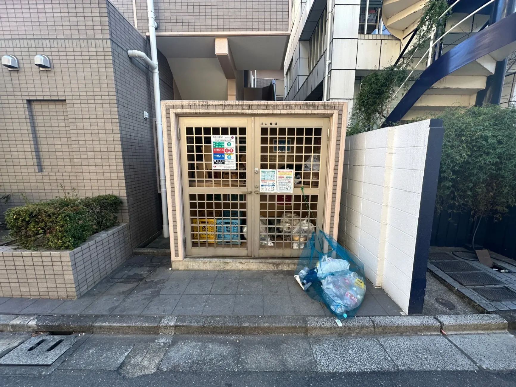 市街地のビル隙間にある古い商店、ポストとごみ袋が外に置かれている外観