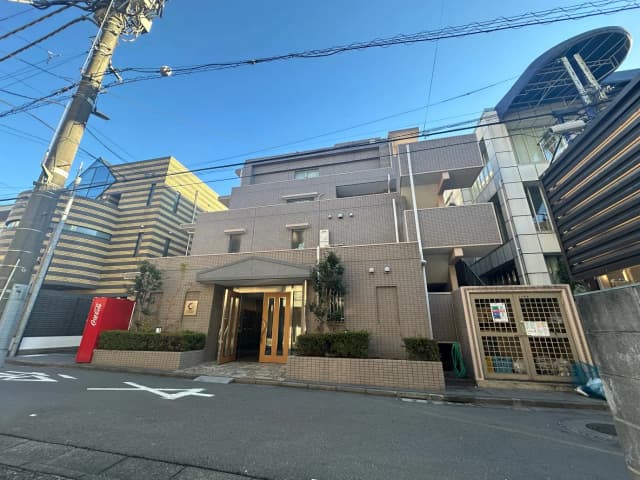 都会の風景、緑色の住宅街に囲まれた現代的な建築物、コカ・コーラの自動販売機が目立つ外観
