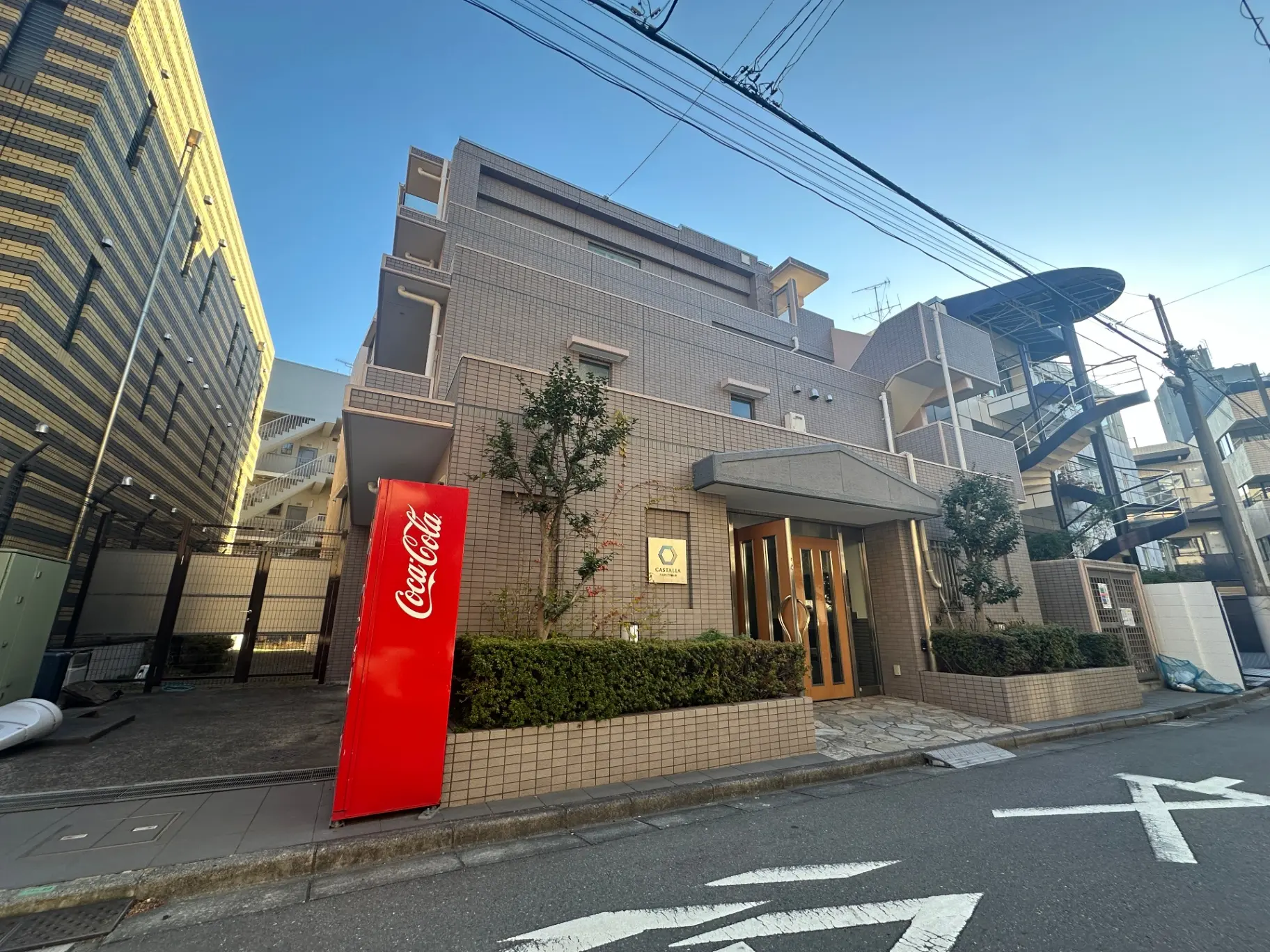 現代的な外観のオフィスビル、コカコーラの看板、歩道沿いに綺麗に整備された緑の植栽