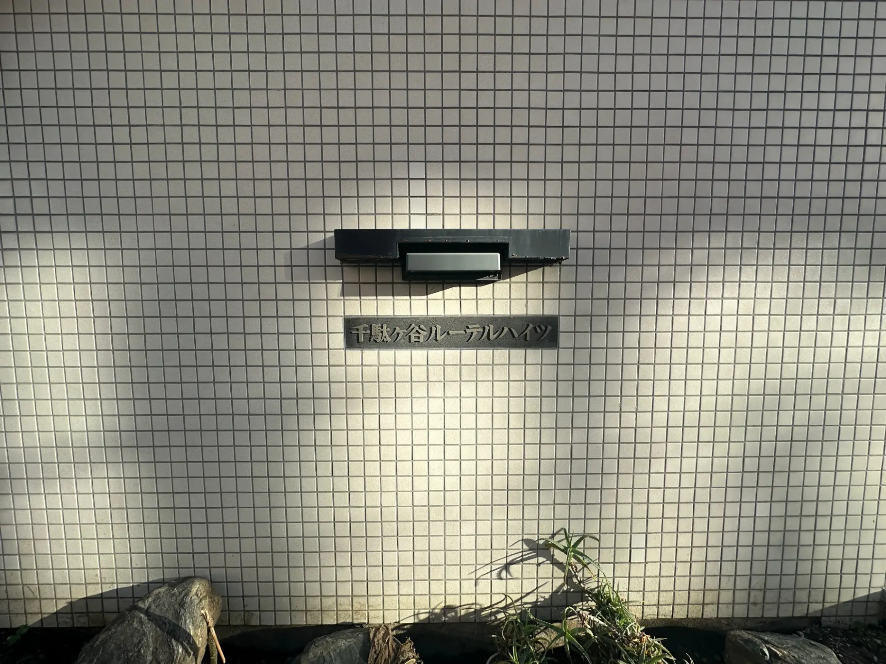 白いタイル壁に取り付けられたポスト、夕日に照らされた郵便受けの影