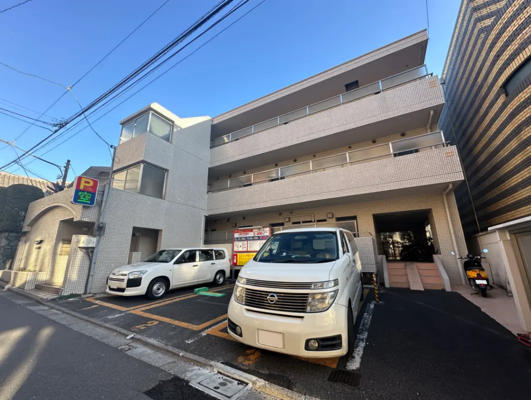 都市のアパートの駐車場、白いタイル張りの建物、道路沿いに停車している車