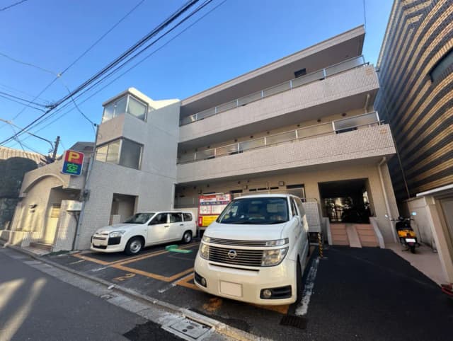 都市のアパートの駐車場、白いタイル張りの建物、道路沿いに停車している車