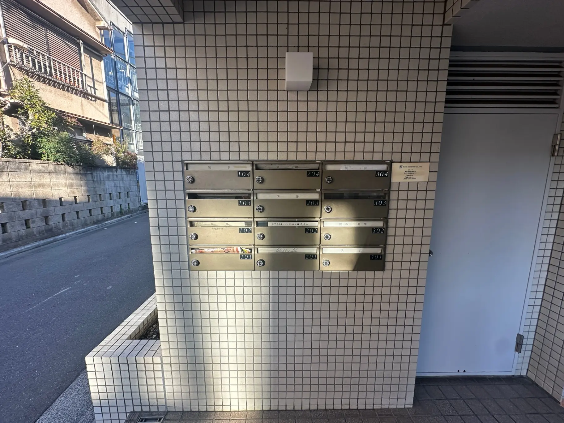 ビルのエントランスに設置された郵便受け、タイル壁、防犯カメラ付き
